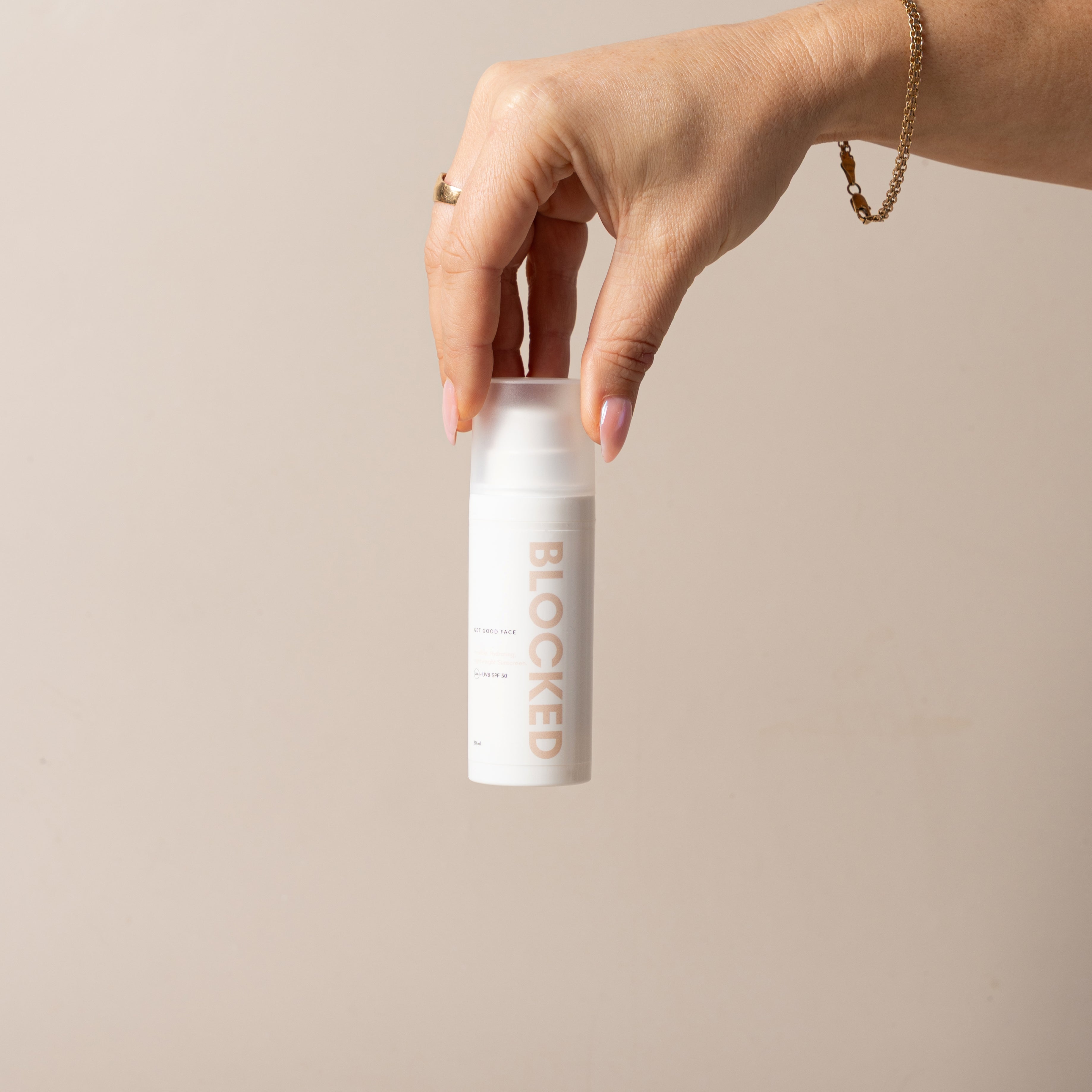 Hand holding a white cylindrical container with 'BLOCKED' branding against a beige background