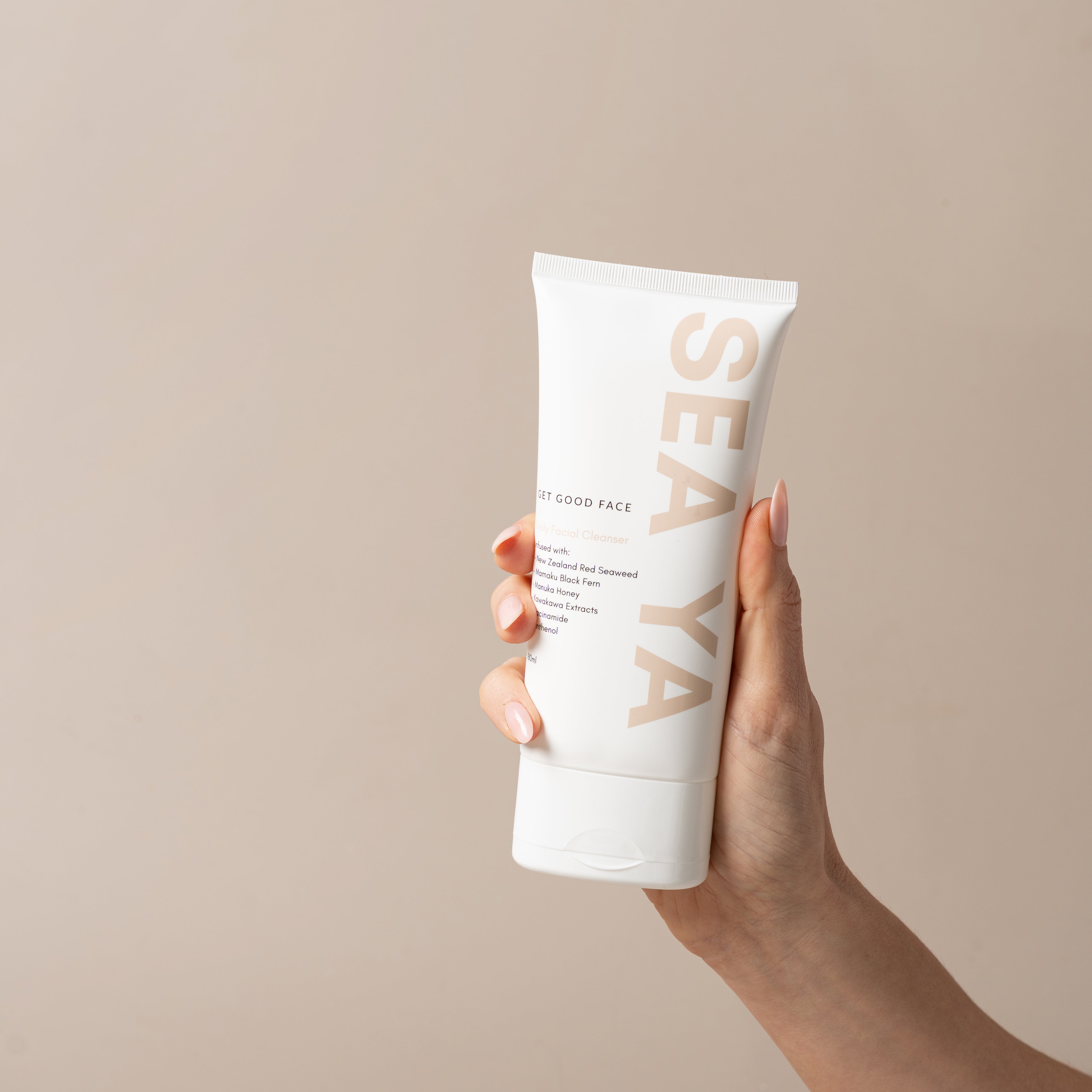 Hand holding a white tube of SEAYA product against a beige background