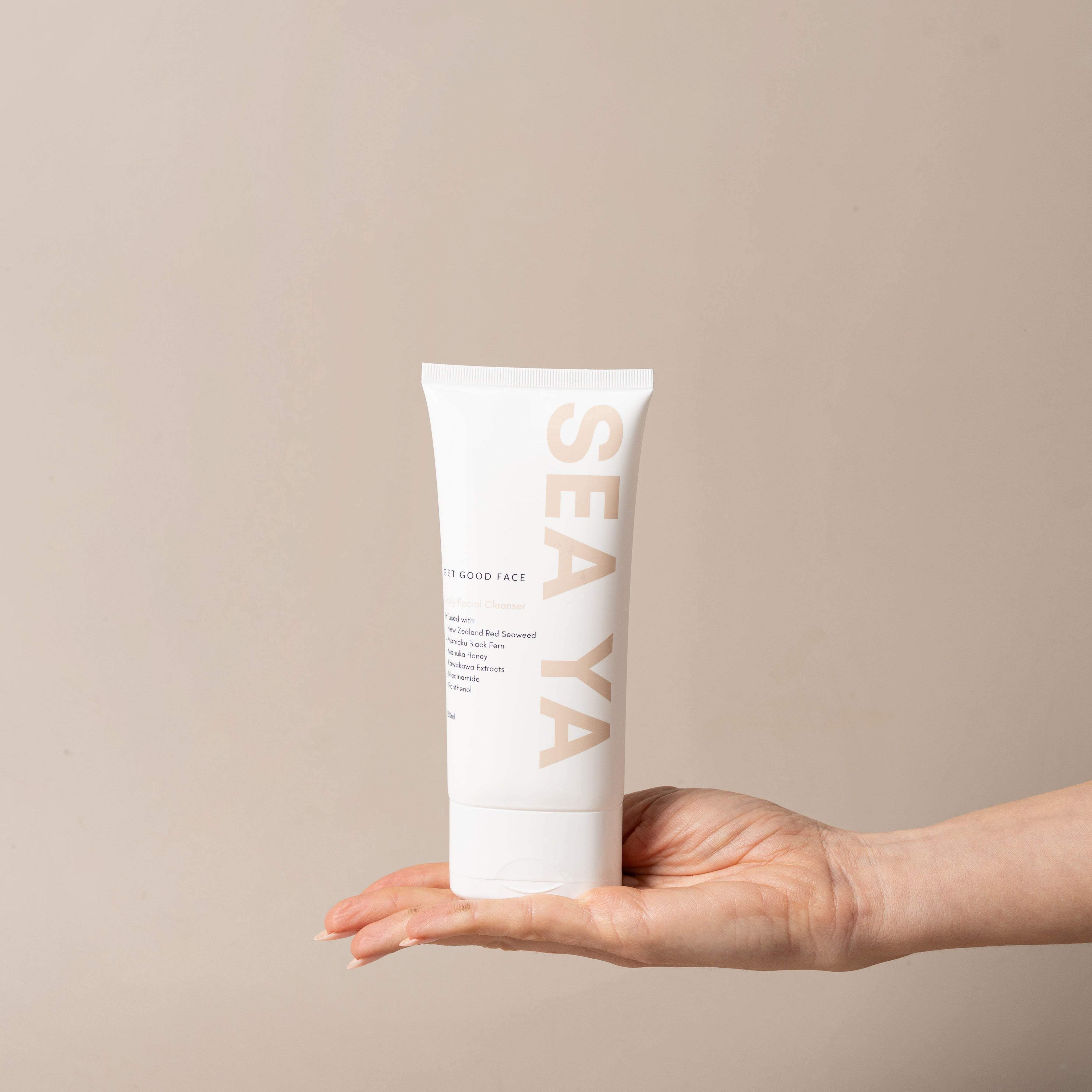 Hand holding a white tube labeled 'SEA YA' against a beige background