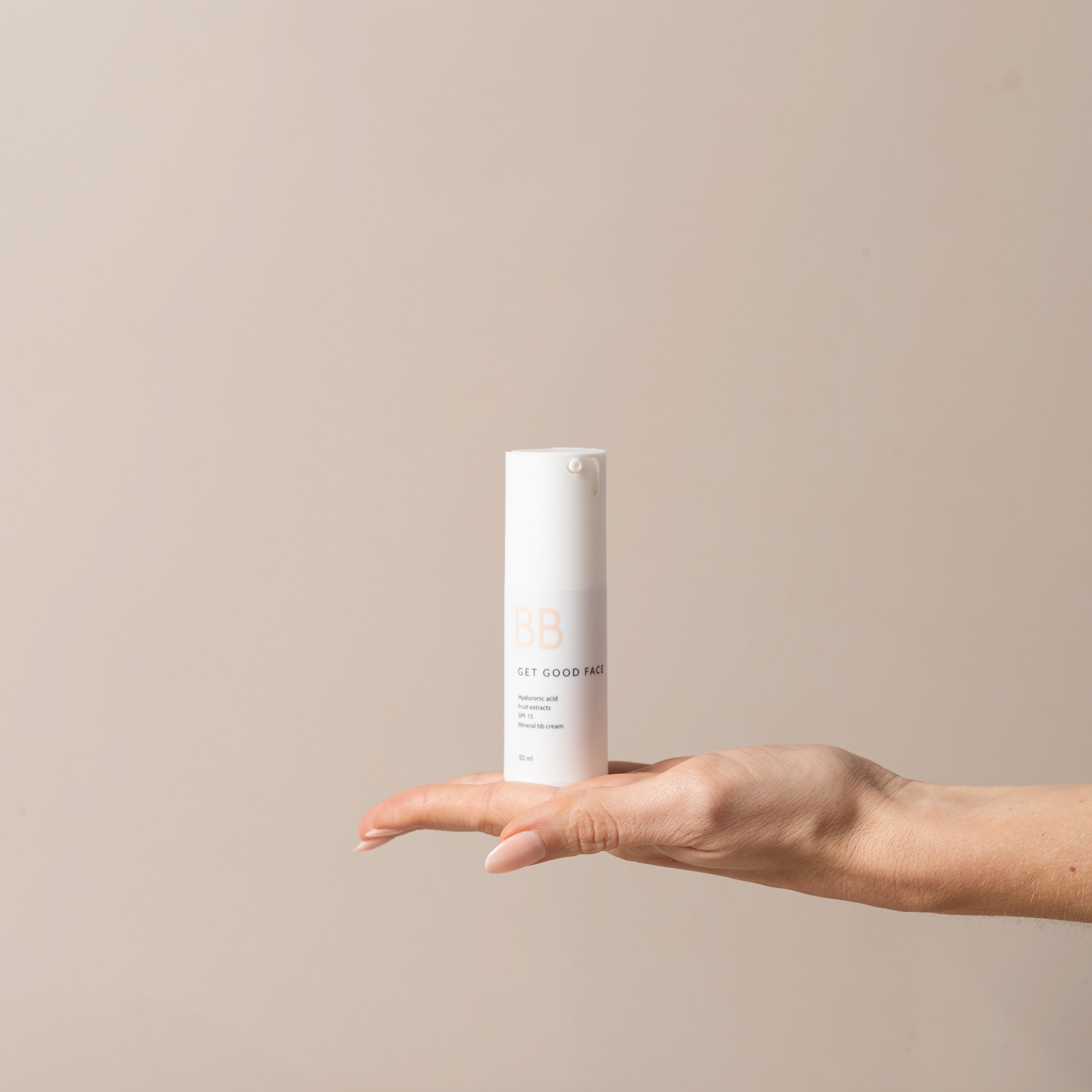 Hand holding a cylindrical skincare product against a beige background