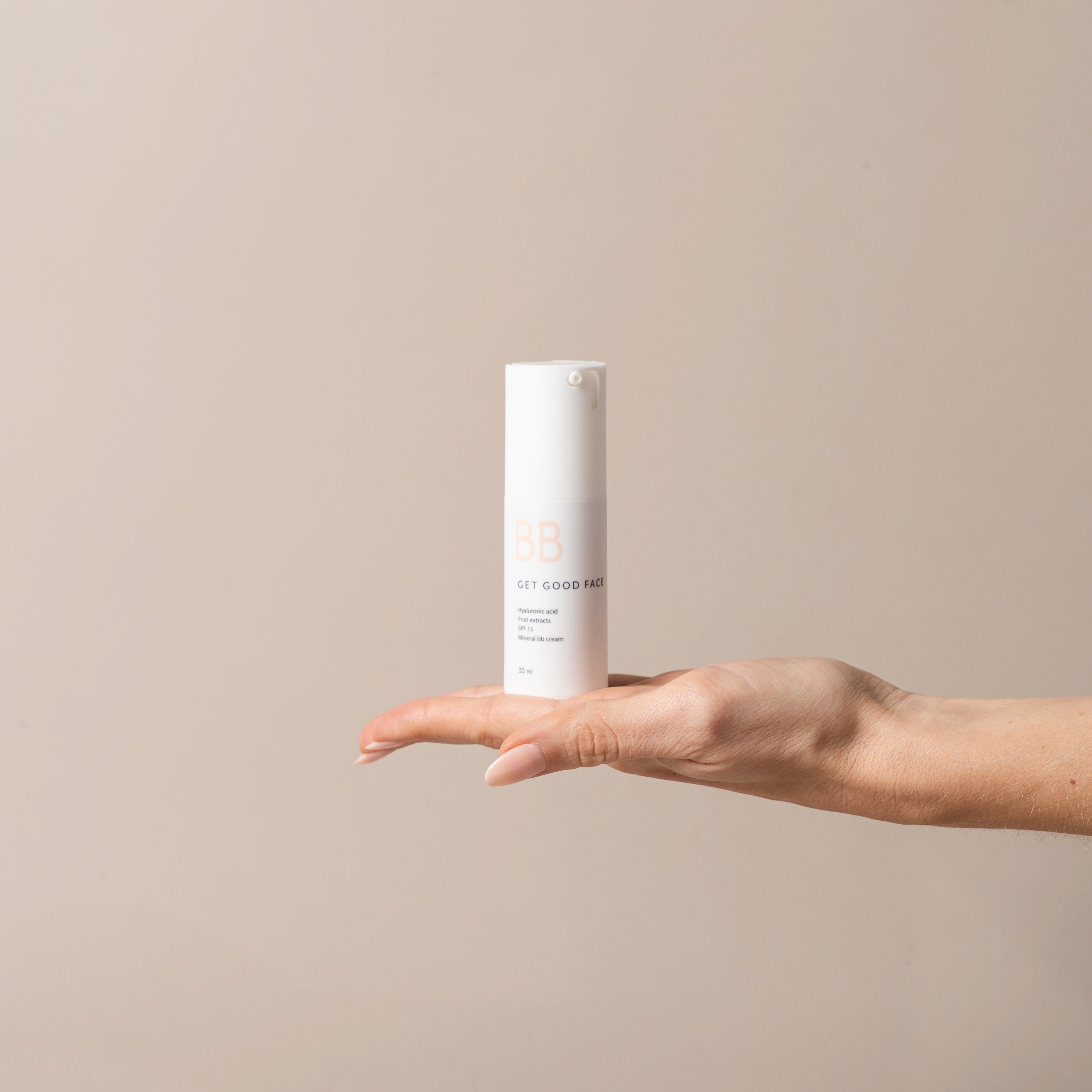 Hand holding a cylindrical skincare product against a beige background