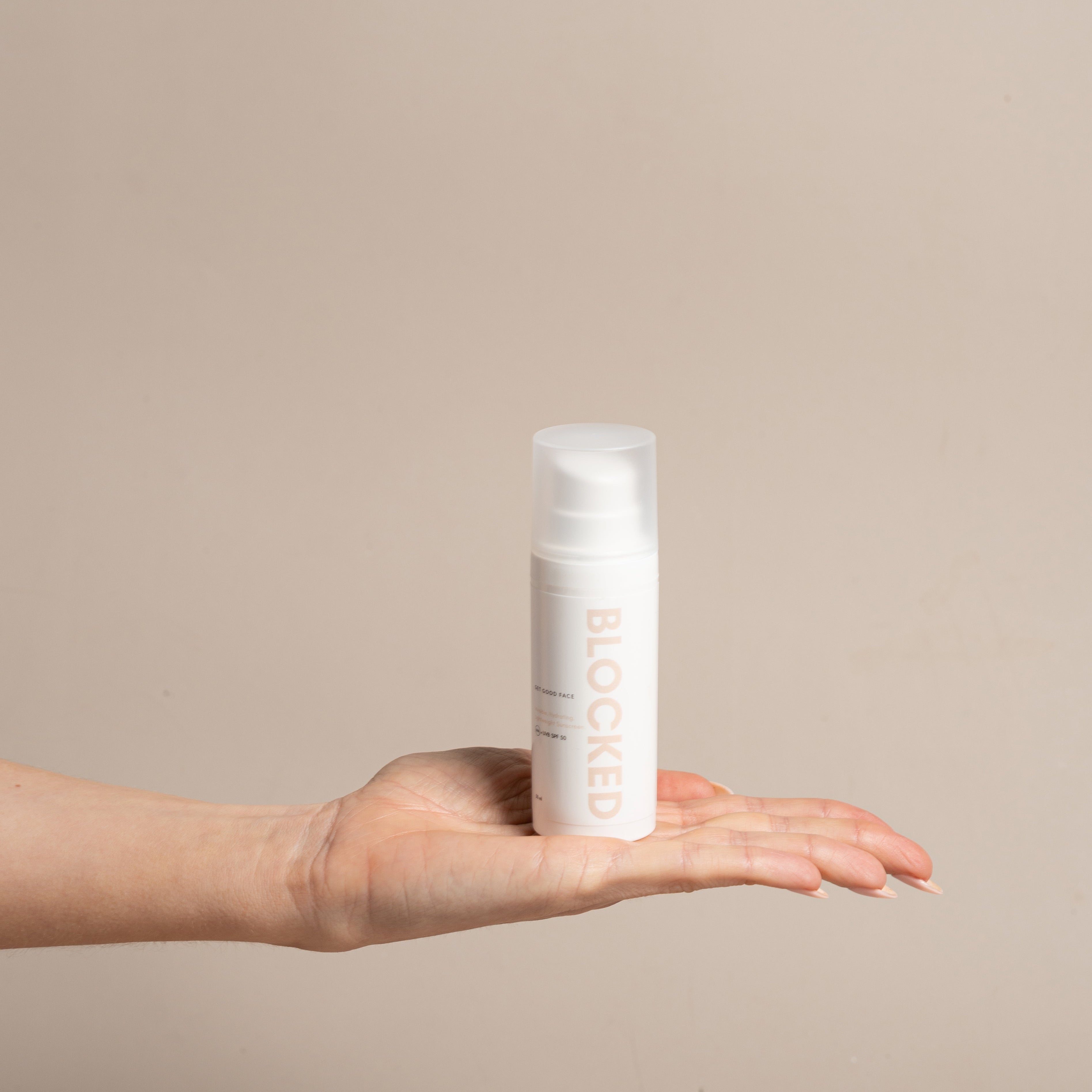 Hand holding a white skincare bottle with text against a beige background
