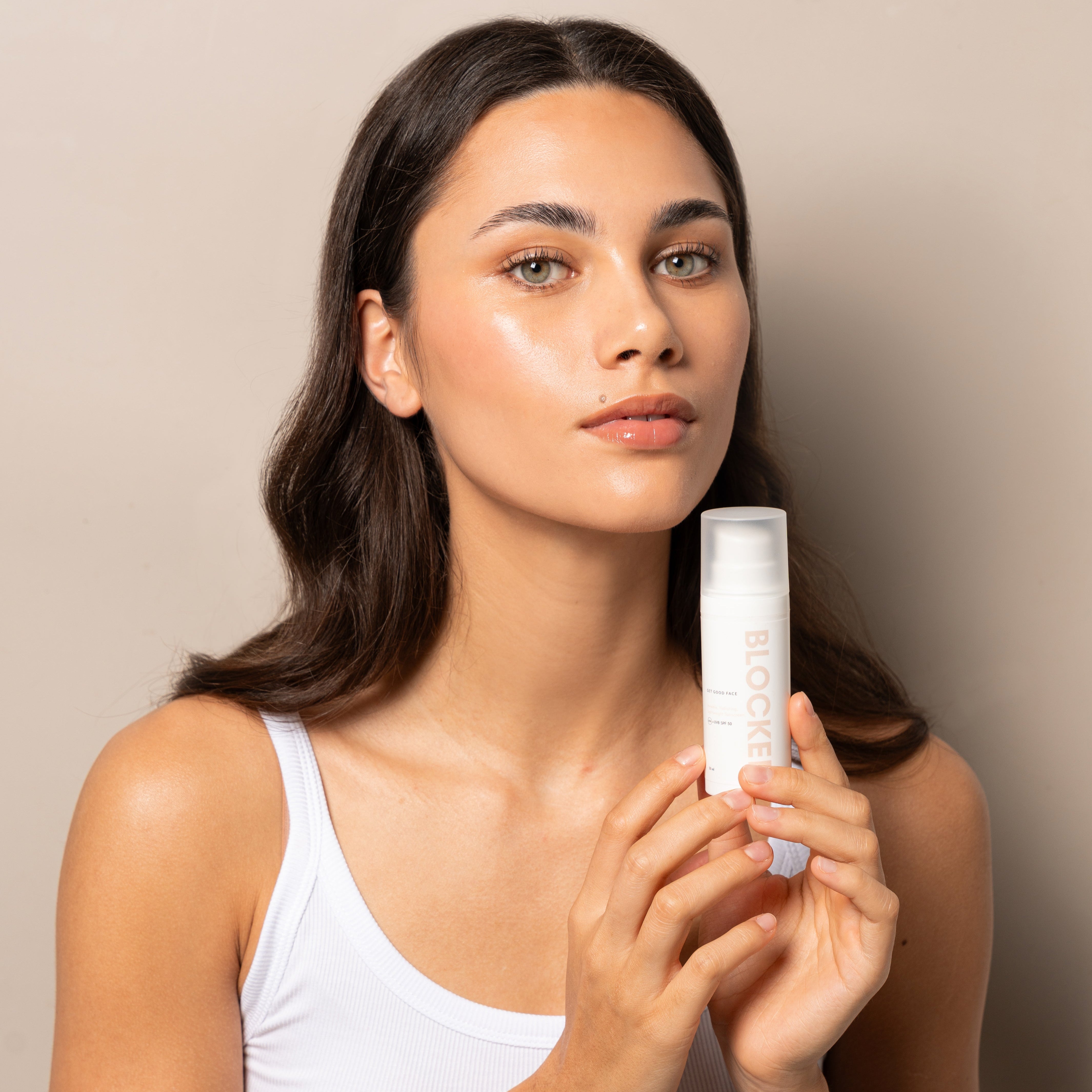 Woman holding a skincare product against a neutral background