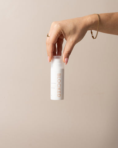 Hand holding a cylindrical product labeled 'BLOCKED' against a beige background