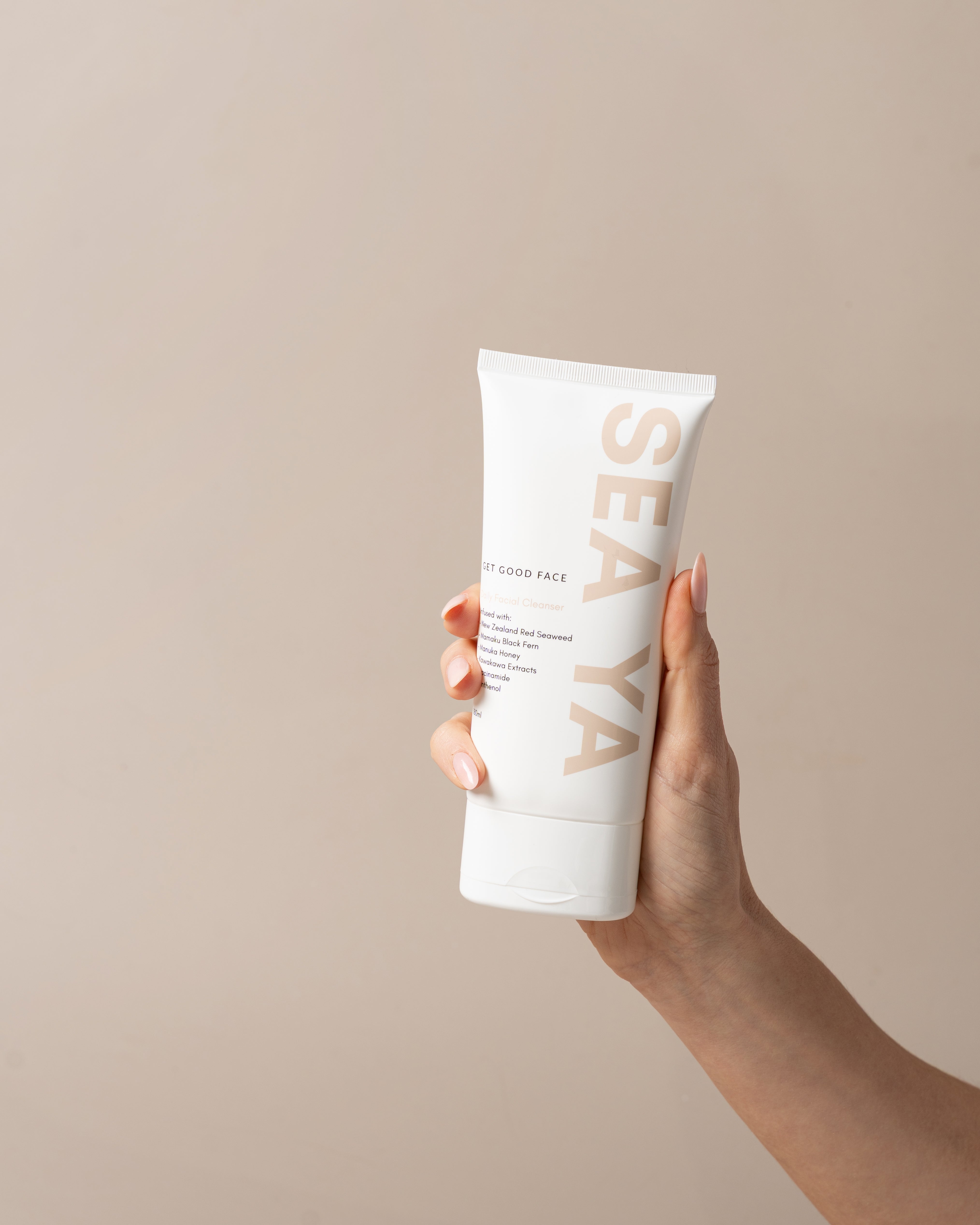 Hand holding a white tube of SEAYA product against a beige background