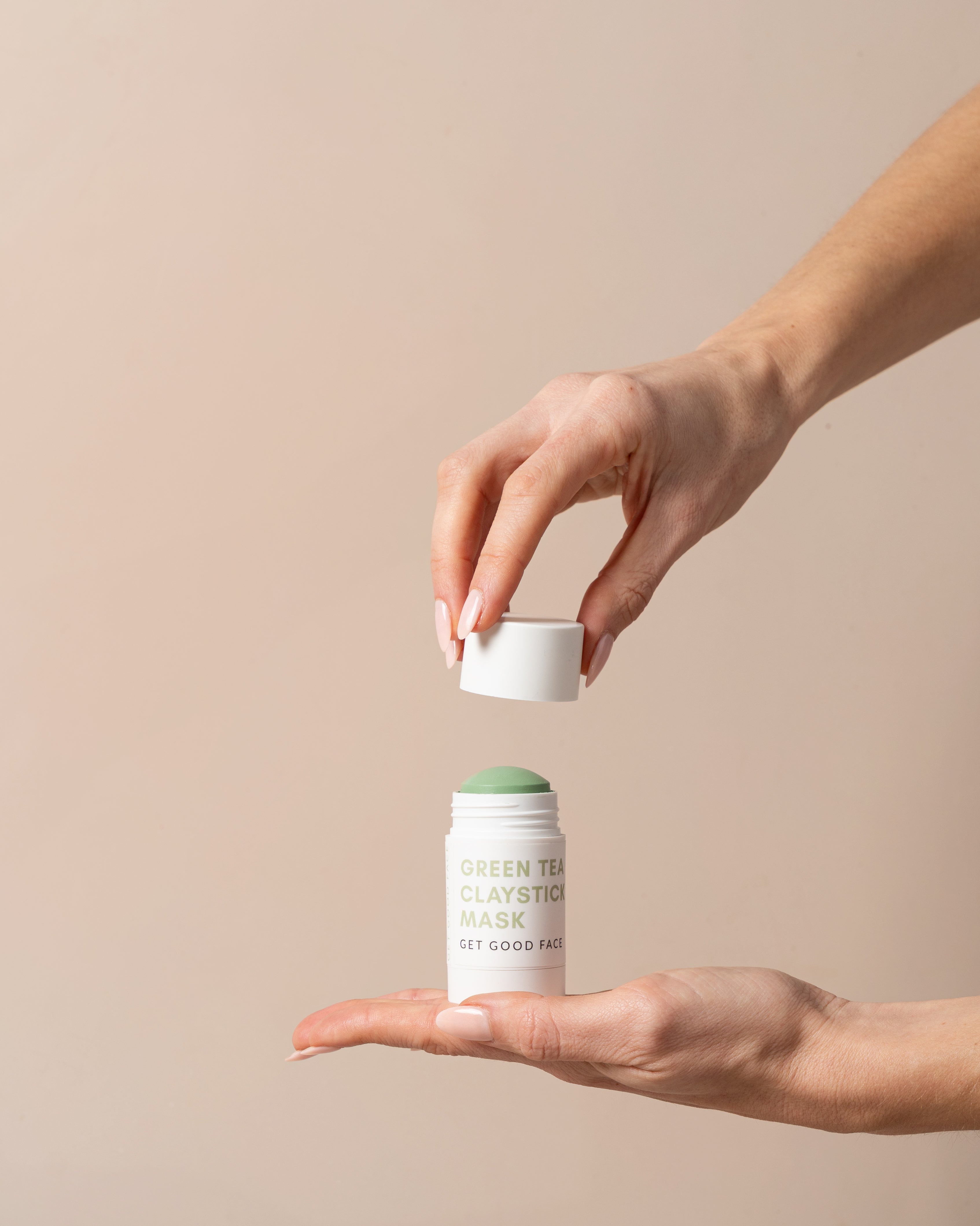 Hand holding a Green Tea Clay stick mask against a beige background