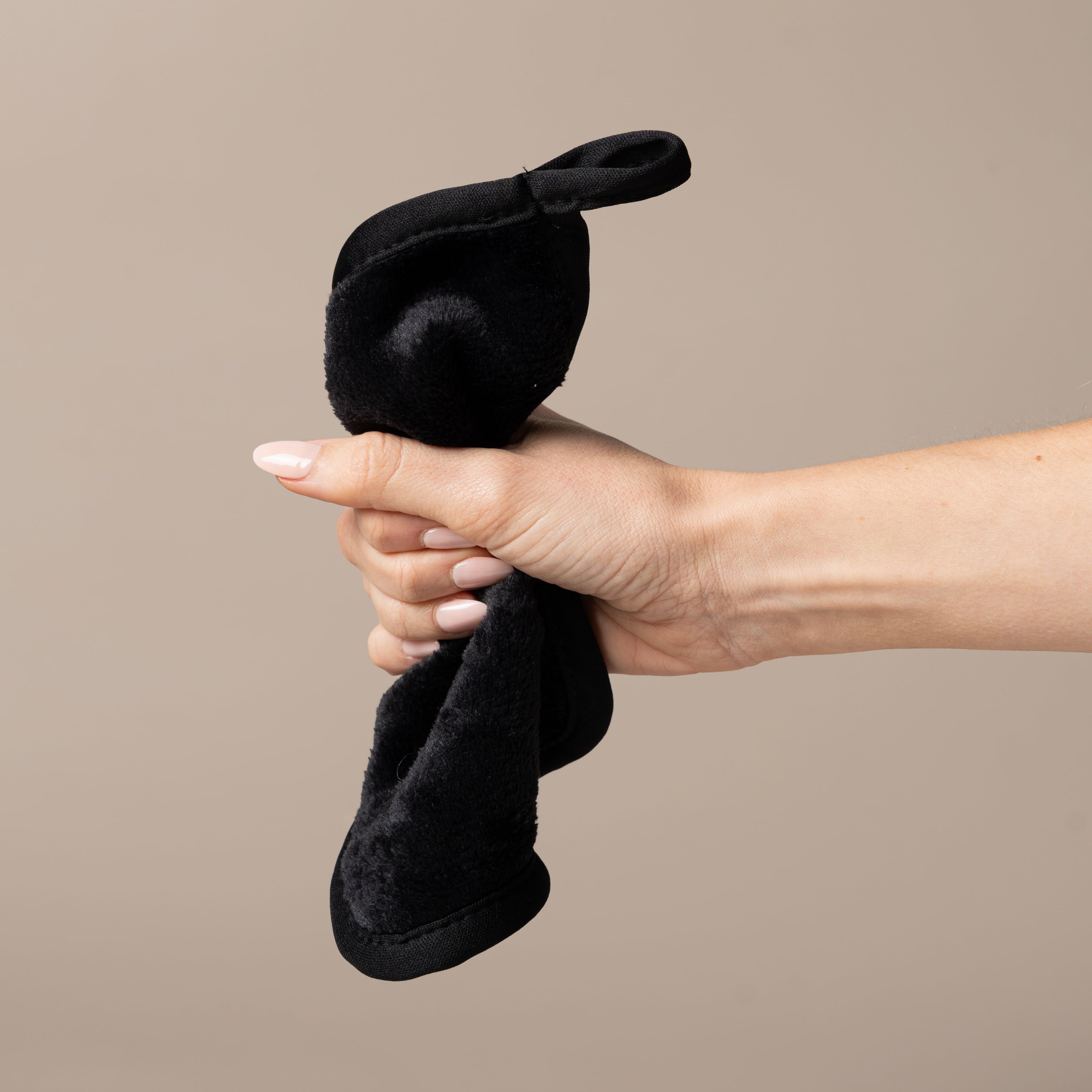 Hand holding a black fur-like product against a beige background