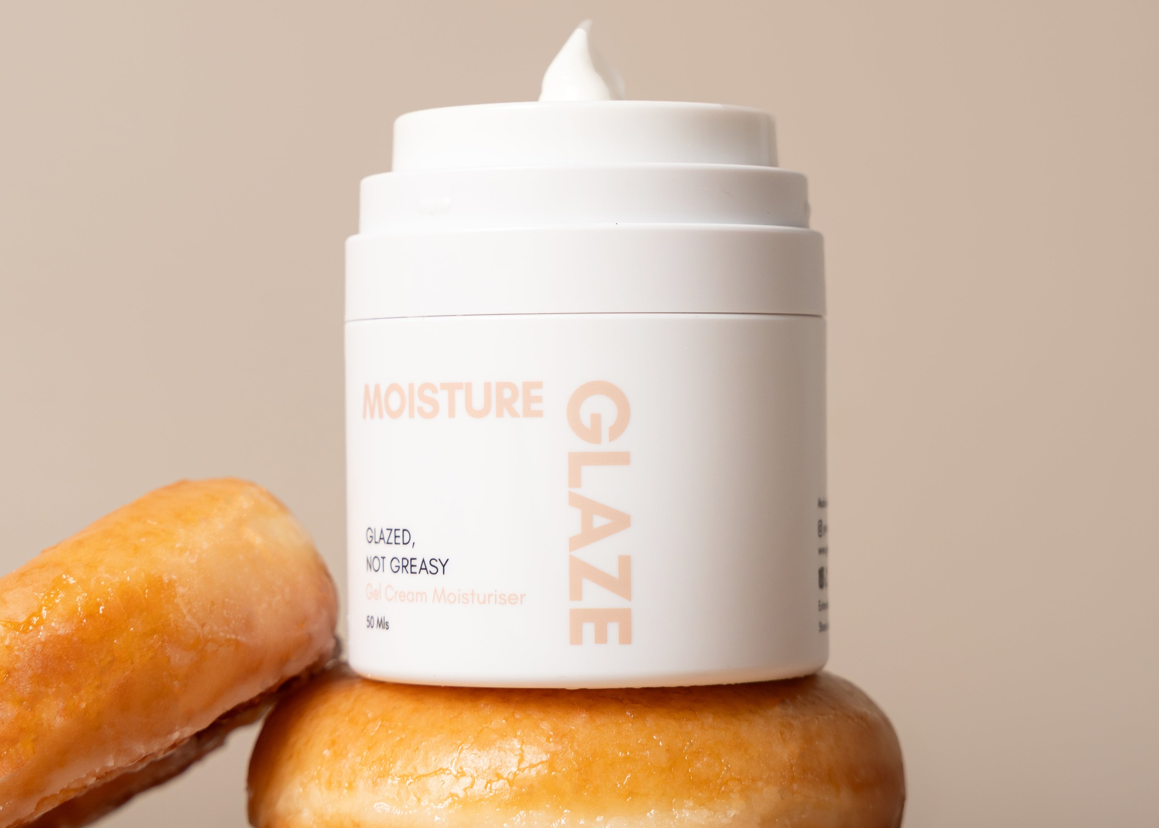 Cream container labeled 'Moisture Glaze' on a stack of glazed donuts with a beige background
