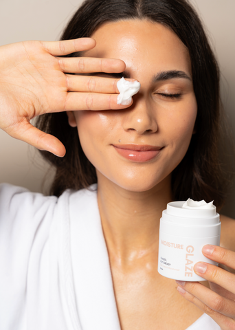 Woman applying cream to her face with a container of the same cream.